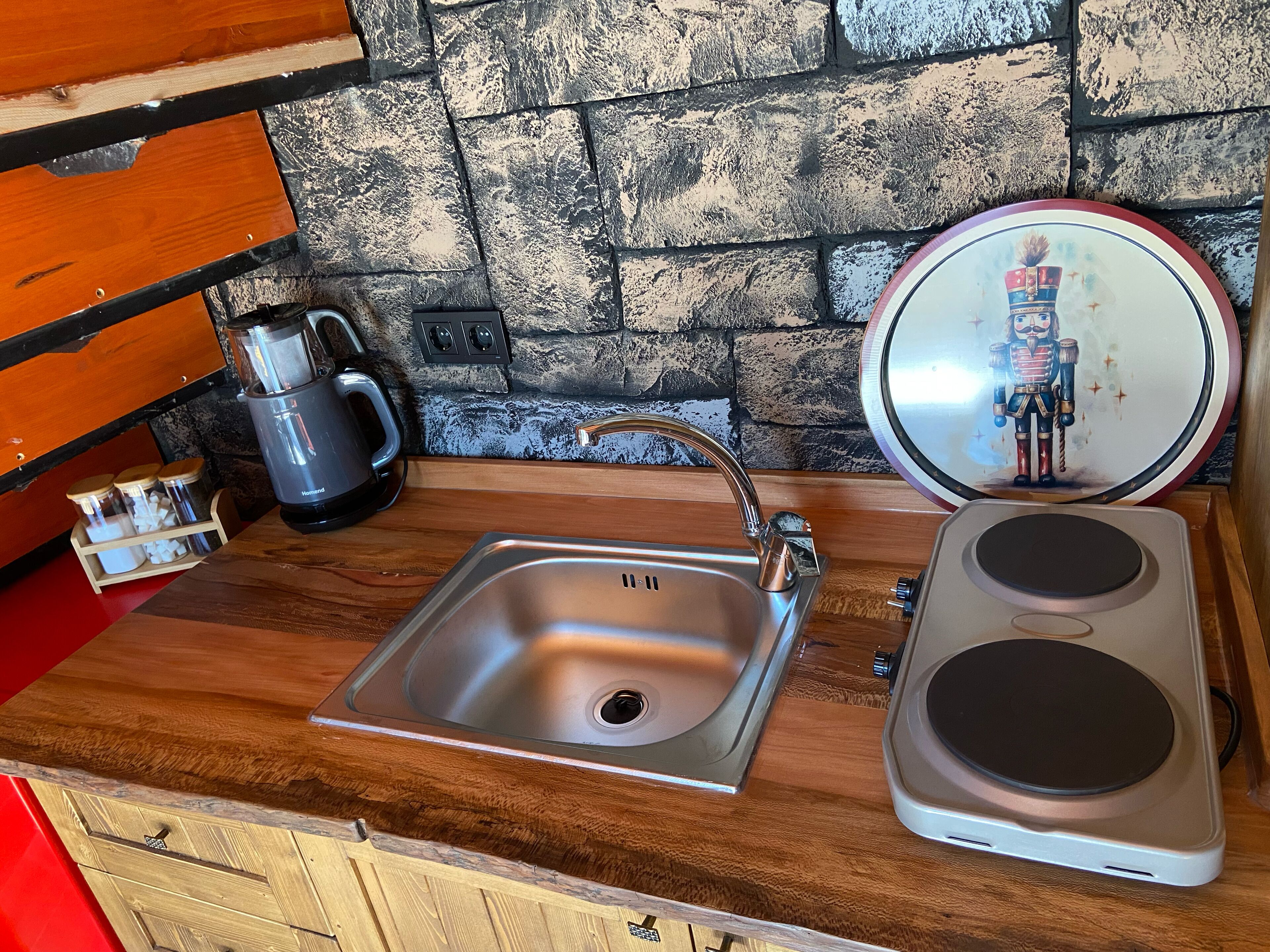 A kitchen with a stainless steel sink, a kettle, and a stove.