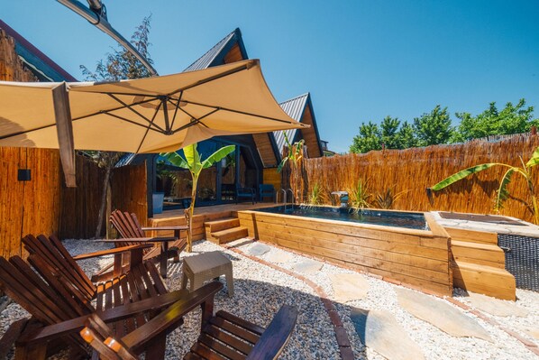 Ein Sitzbereich im Freien mit Holzbänken und einem großen Sonnenschirm, einer Holzterrasse und einem kleinen Pool.