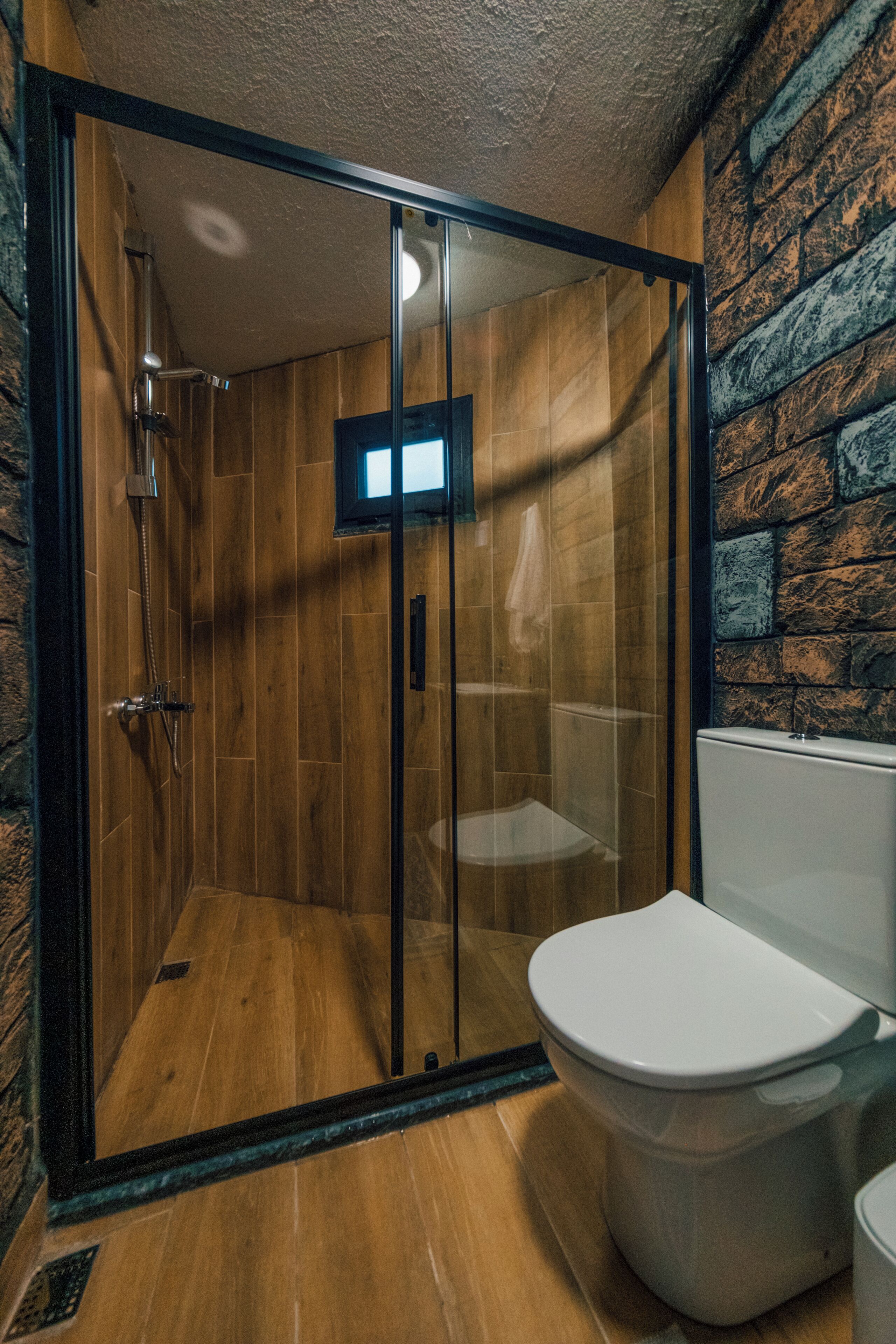 A bathroom with a wooden floor, a white toilet, and a glass-enclosed shower area.