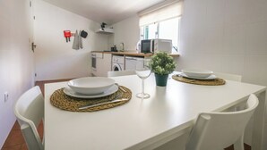 Una cocina moderna con electrodomésticos blancos, una mesa de comedor con platos y un vaso, y una planta en maceta sobre la encimera.