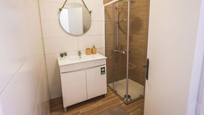 Un baño moderno con ducha de vidrio, un espejo redondo y un lavabo blanco con una pequeña planta.
