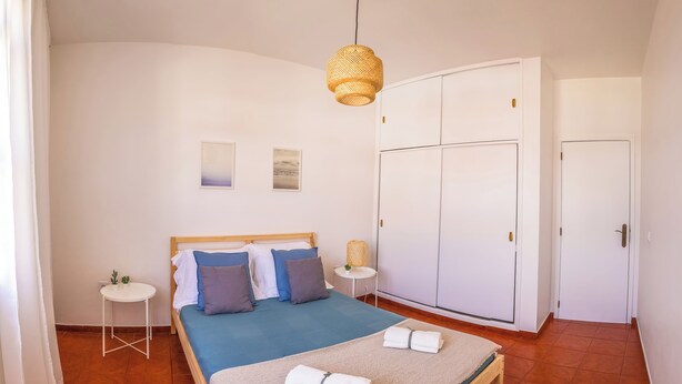 Un dormitorio con cama, mesitas de noche, armario e iluminación colgante.