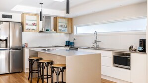 Una cocina moderna con una isla central, taburetes de bar, horno empotrado y cafetera.