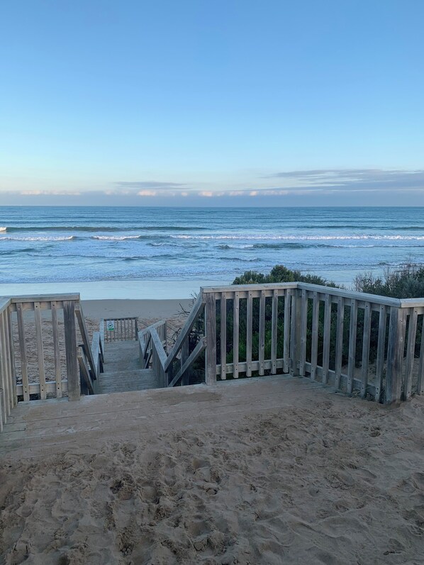 A wooden boardwalk leading to a sandy beach with ocean waves in the background.