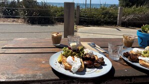 A meal on a wooden table with a view of the sea and a sign in the background. - Ideally located Beach House close to picturesque reserve and beaches (Torquay)