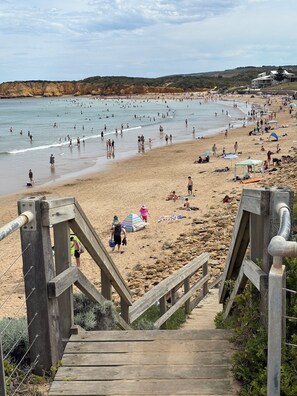 A beach with a wooden staircase leading down to the shore, surrounded by rocks and sparse vegetation. - Torquay Beach Escape • 400m to the Beach (Torquay)