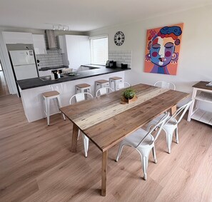 Een moderne keuken met witte kasten, een zwart aanrecht en een houten eettafel met witte stoelen.