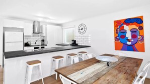 A modern kitchen with white cabinets, a black countertop, and a wooden dining table with white chairs. - Ideally located Beach House close to picturesque reserve and beaches (Torquay)
