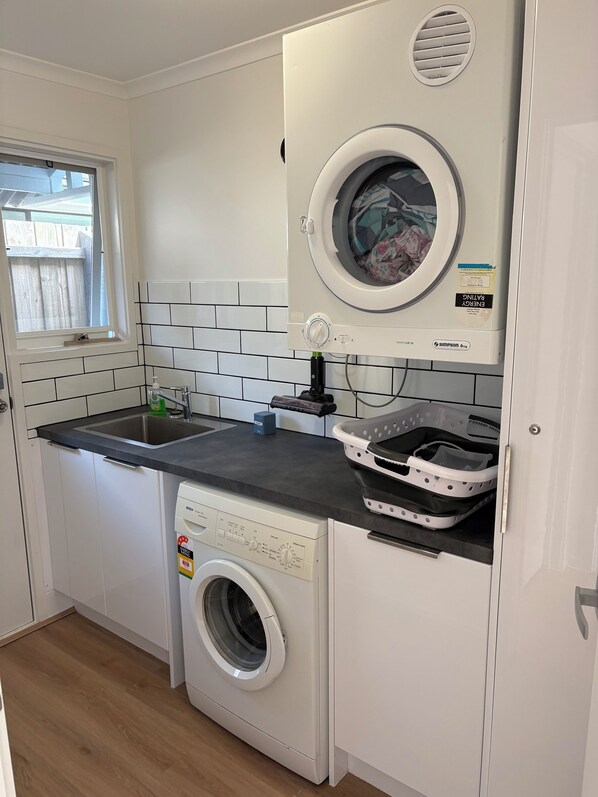 A compact laundry room with a front-loading washing machine, a dryer, a sink, and a window. - Torquay Beach Escape • 400m to the Beach (Torquay)