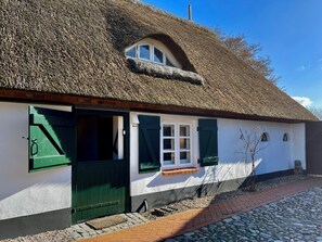A traditional thatched-roof cottage with a white exterior, green shutters, and a small window.