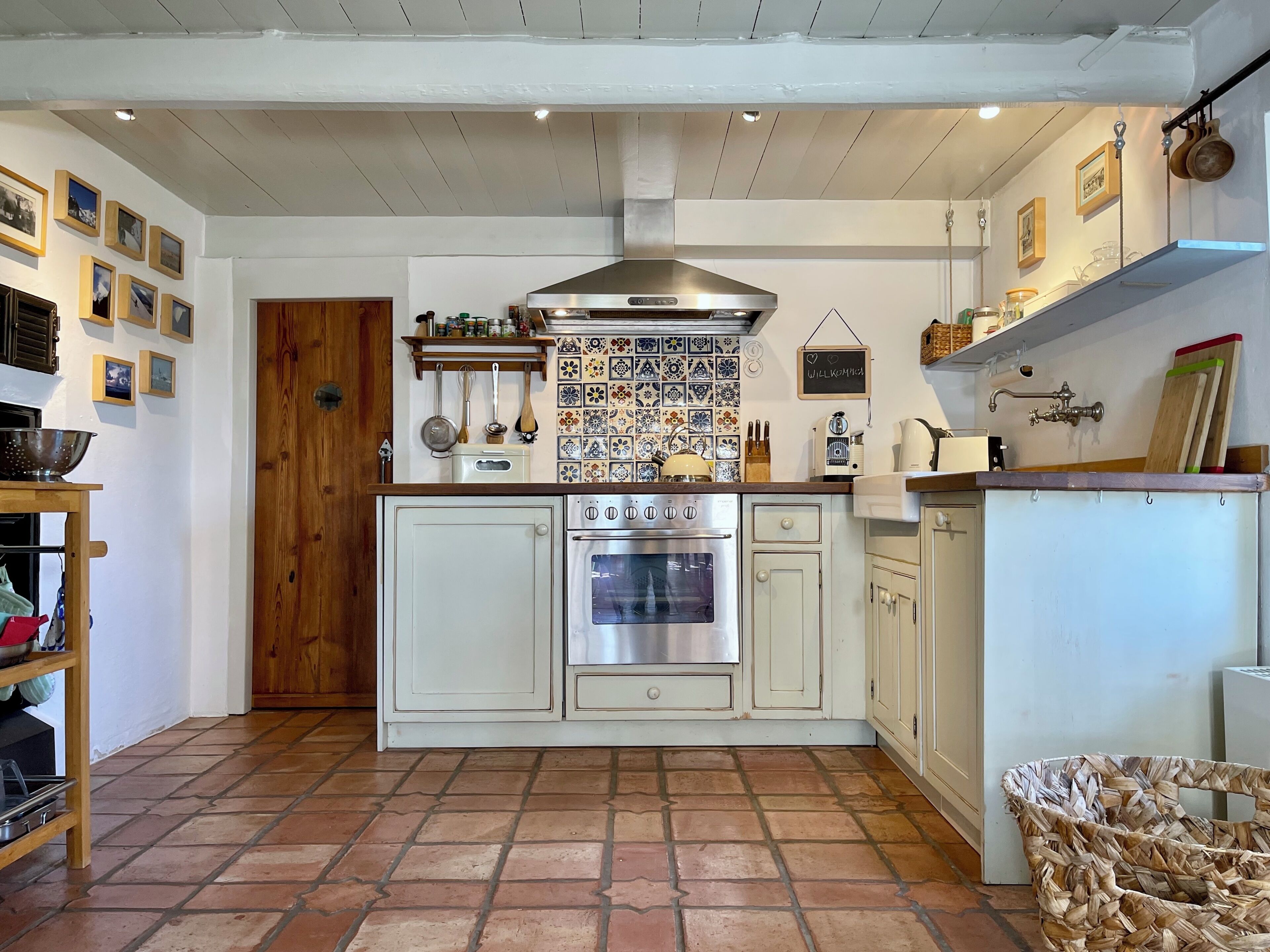 A kitchen with white cabinets, a stainless steel oven, a hanging pot rack, and a tiled backsplash.