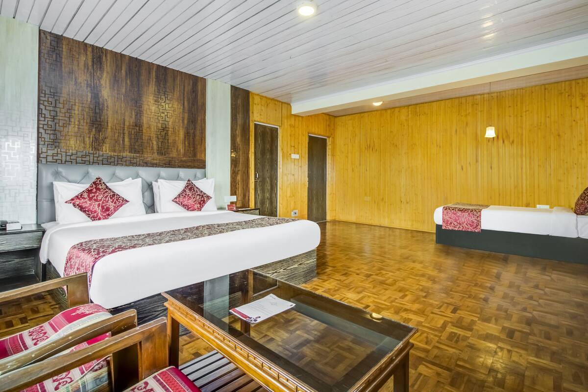 A hotel room with a large bed, a sofa, a glass coffee table, and wooden flooring.
