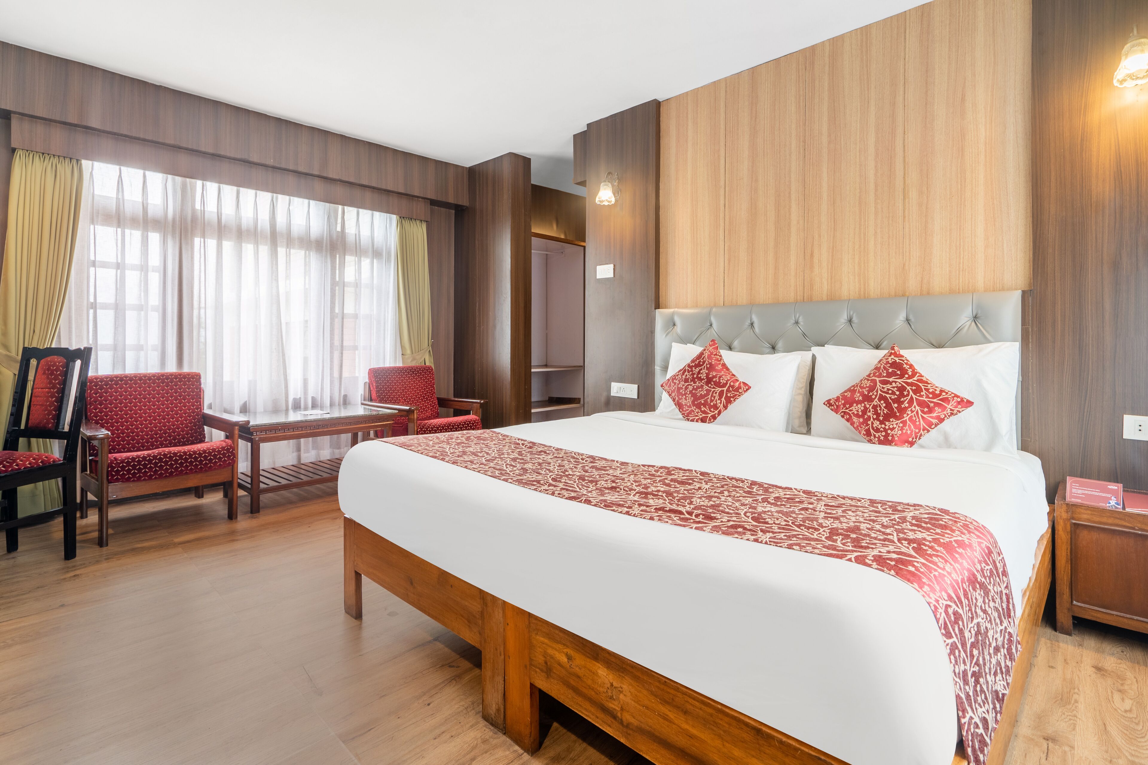 A hotel room with a large bed, a wooden headboard, a desk with a chair, and a wardrobe.