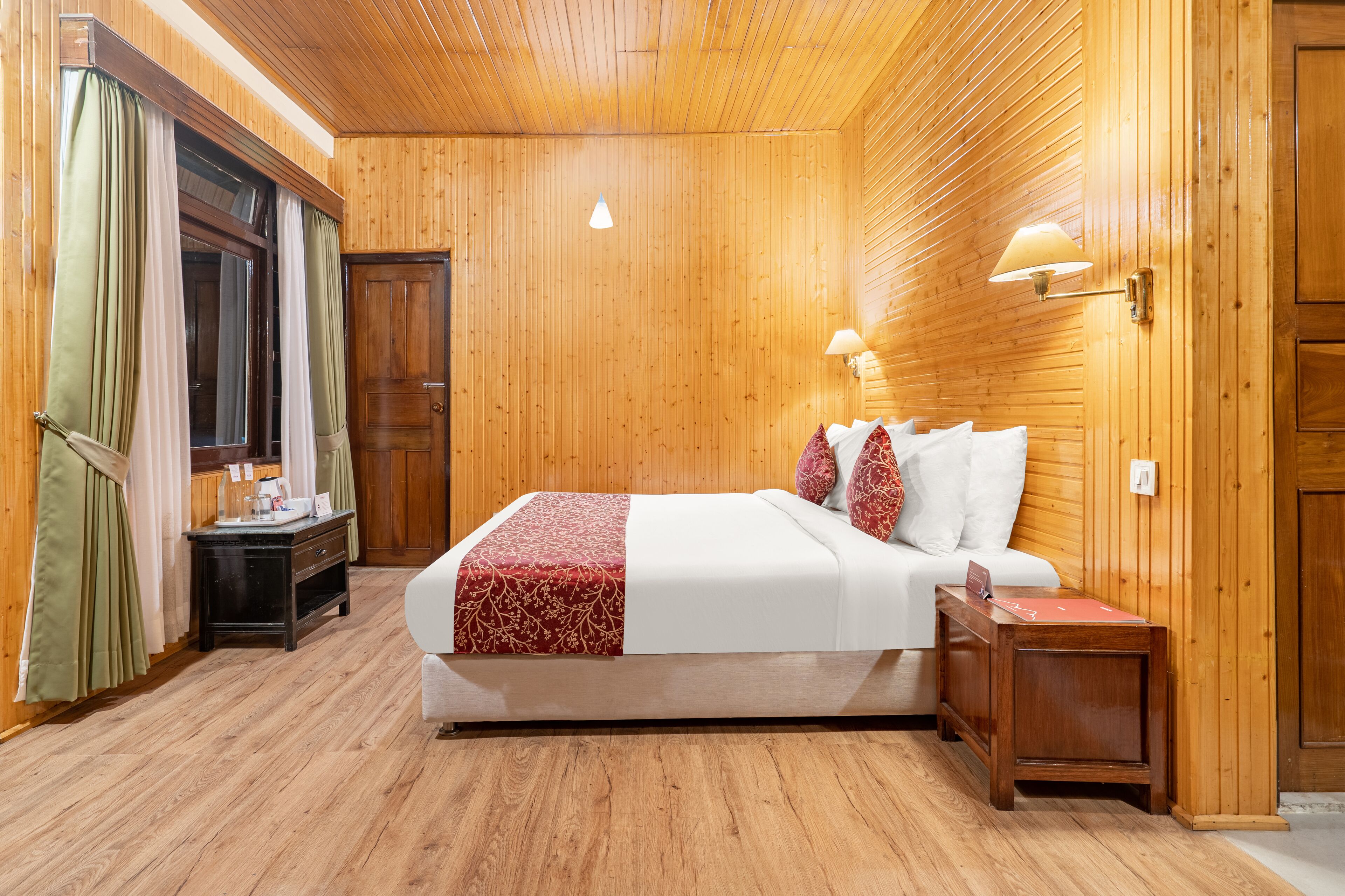 Quarto com painéis de madeira, uma cama, mesas de cabeceira e uma janela com cortinas.