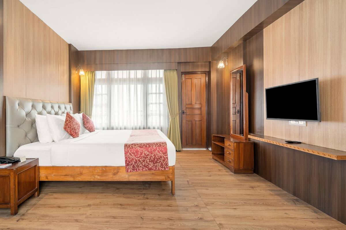 A hotel room with a large bed, wooden flooring, a TV mounted on the wall, and a wooden wardrobe.