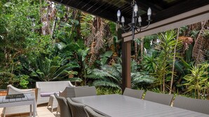 An outdoor patio with wicker furniture and a table, surrounded by lush tropical plants. - San Lameer Villa 2810 (Southbroom)