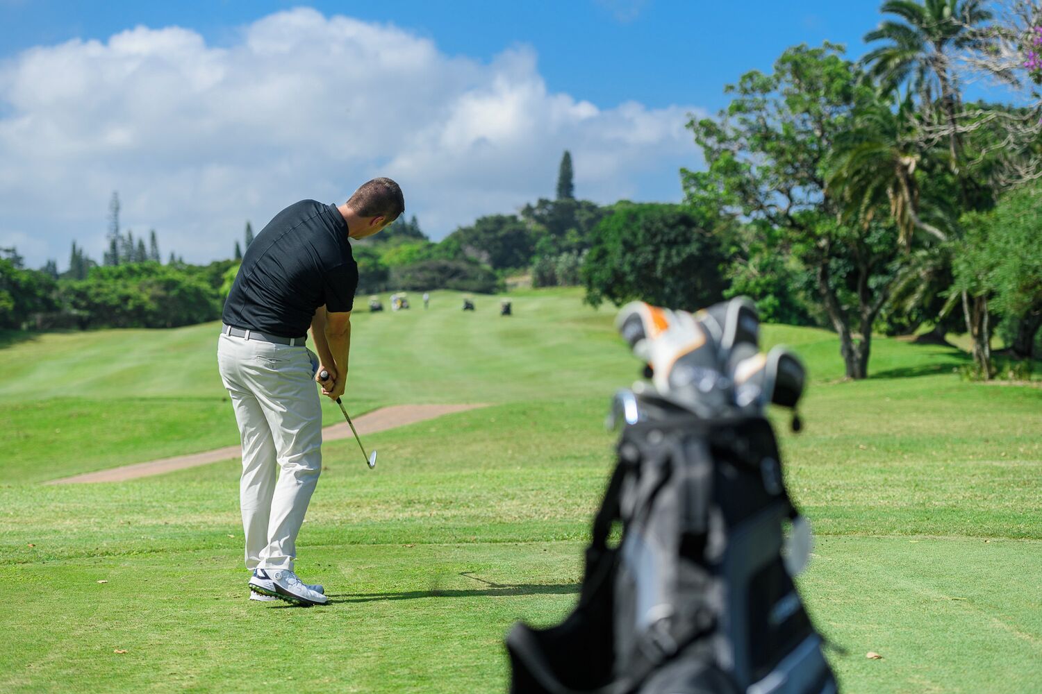 A golf course with a golfer preparing to take a shot, a golf bag, and a clear sky.