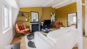 Un salon moderne avec un canapé blanc, un fauteuil rouge, une cheminée et un téléviseur.