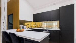 Une cuisine moderne avec des meubles noirs, un plan de travail blanc et un four encastré. On y trouve un panier de fruits sur le plan de travail et une chaise noire.