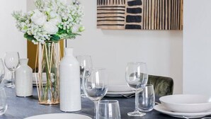 Une table à manger dressée avec de l’assiette blanche, des verres et un vase contenant des fleurs blanches.