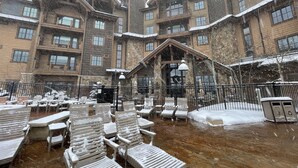 Un'area salotto esterna coperta di neve, con diverse poltrone e tavoli, circondata da un edificio con molti balconi e finestre.