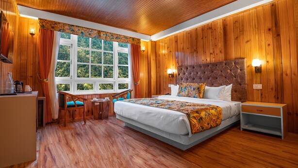 A wooden-paneled room with a large bed, a desk, and a chair. - Summit Gangchen Hotel (Chungthang)