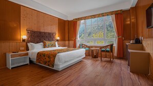 A wooden-paneled room with a bed, bedside tables, a small table, and a chair. - Summit Gangchen Hotel (Chungthang)