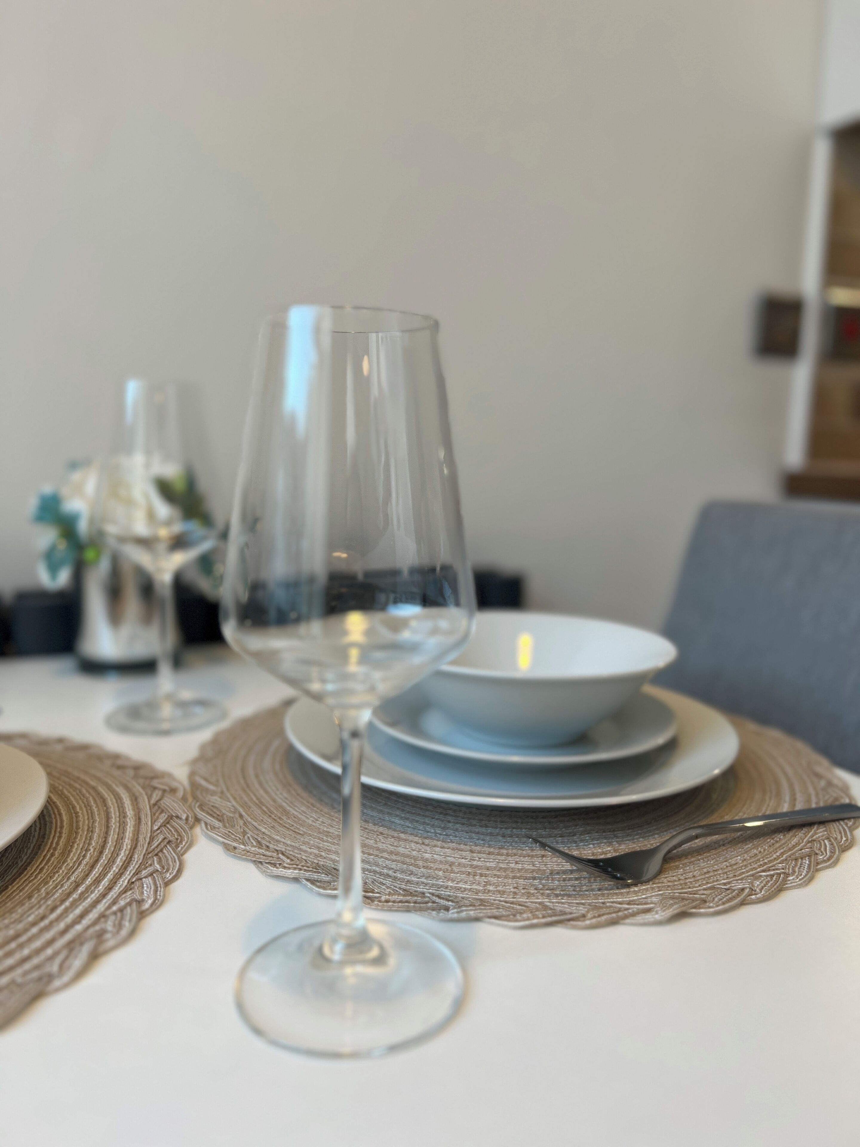 A dining table with a wine glass, plates, and a bowl.