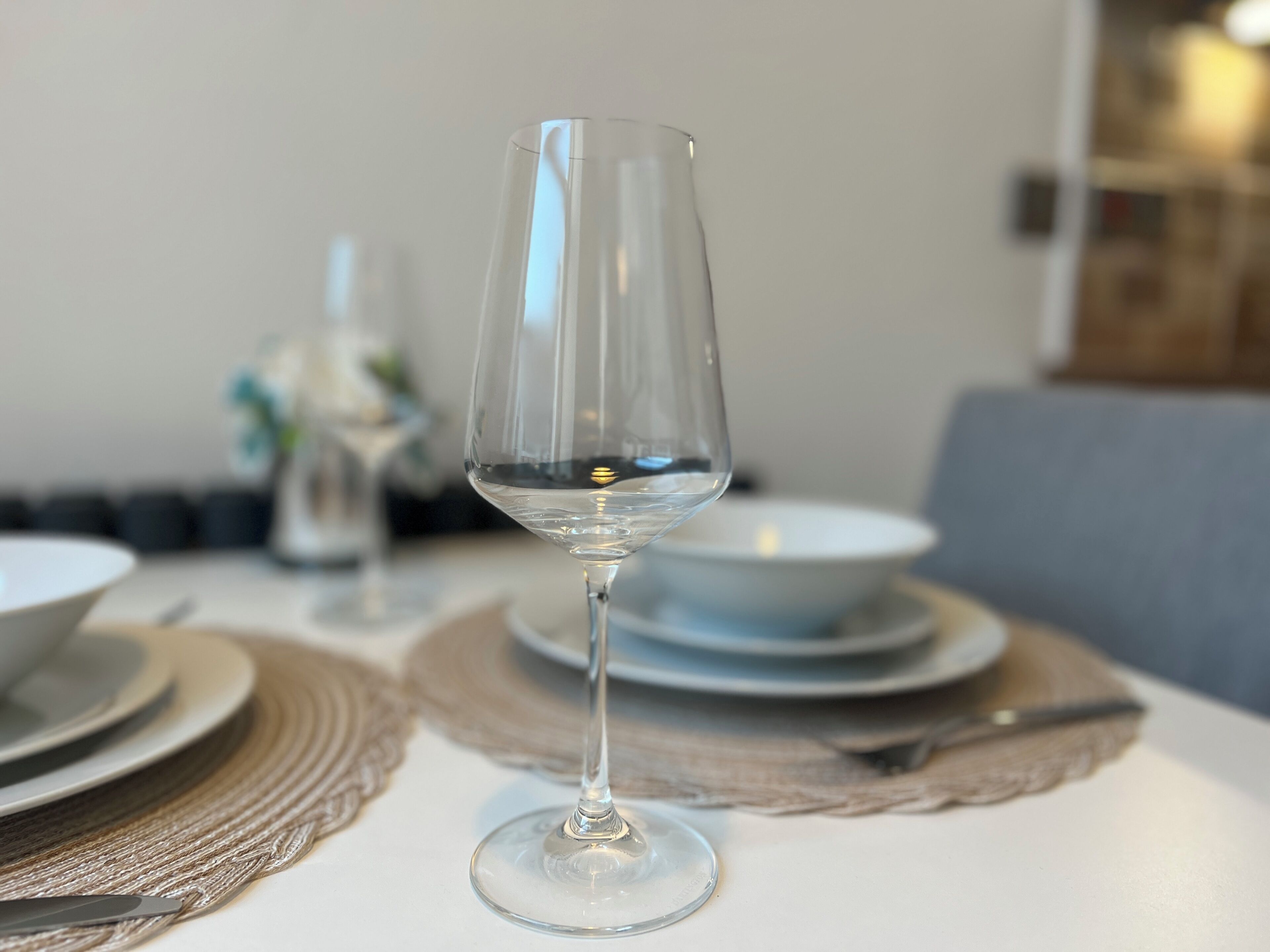 Un verre à vin transparent, posé sur une table recouverte d’une nappe, entouré d’assiettes et d’un saladier.