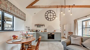 Eine moderne Küche mit einer zentralen Kochinsel, einem Essbereich mit rundem Tisch und Stühlen sowie einem Wohnbereich mit einer Couch und einem Couchtisch.