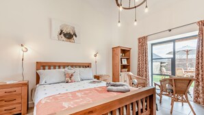 Ein Schlafzimmer mit einem hölzernen Bett, Nachttischen, einem Schrank aus Holz, einem Korbstuhl und einem Balkon mit Aussicht.