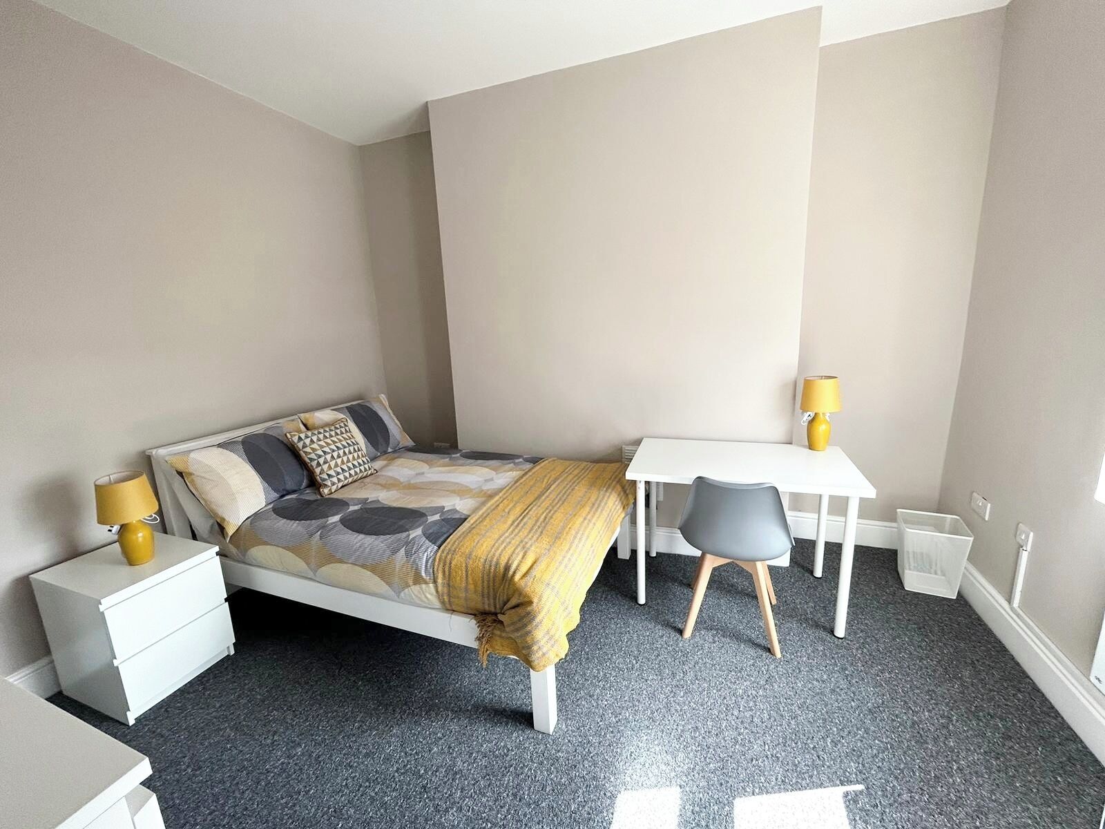 A bedroom with a bed, bedside tables, a desk, and a chair.