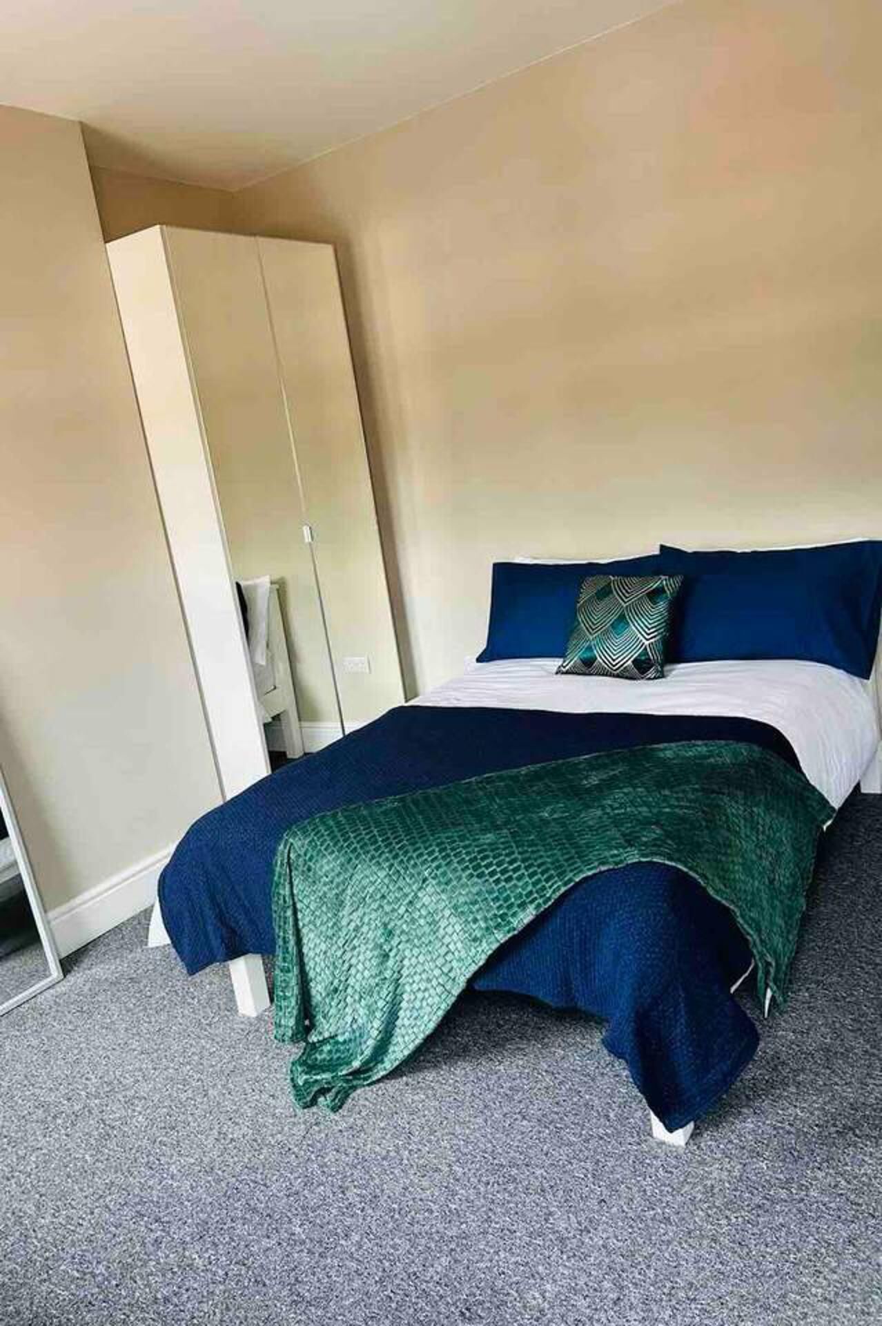 A hotel room with a bed, a green throw blanket, a blue pillow, and a wardrobe.