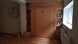 Una habitación con un armario de madera, un reloj en la pared y una ventana con vistas.