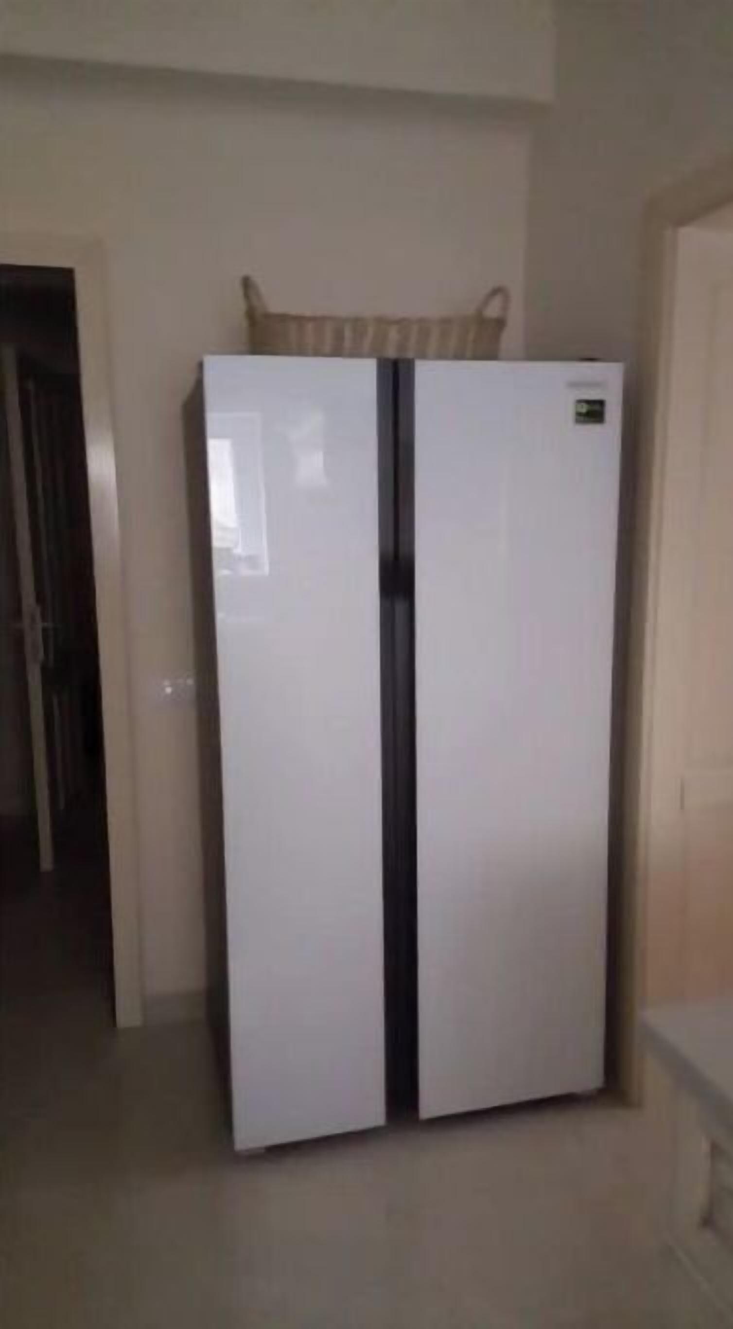 A white refrigerator with a freezer compartment, placed in a room with a tiled floor and a door on the right.