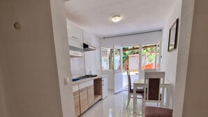 A kitchen with white cabinets, a stove, and a dining area with a table and chairs. - Four Bedroom apt w Patio Close to Beach and Center (Hvar)