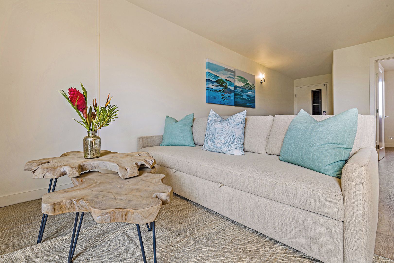 A living room with a sofa, a coffee table with a vase of flowers, and a painting on the wall.