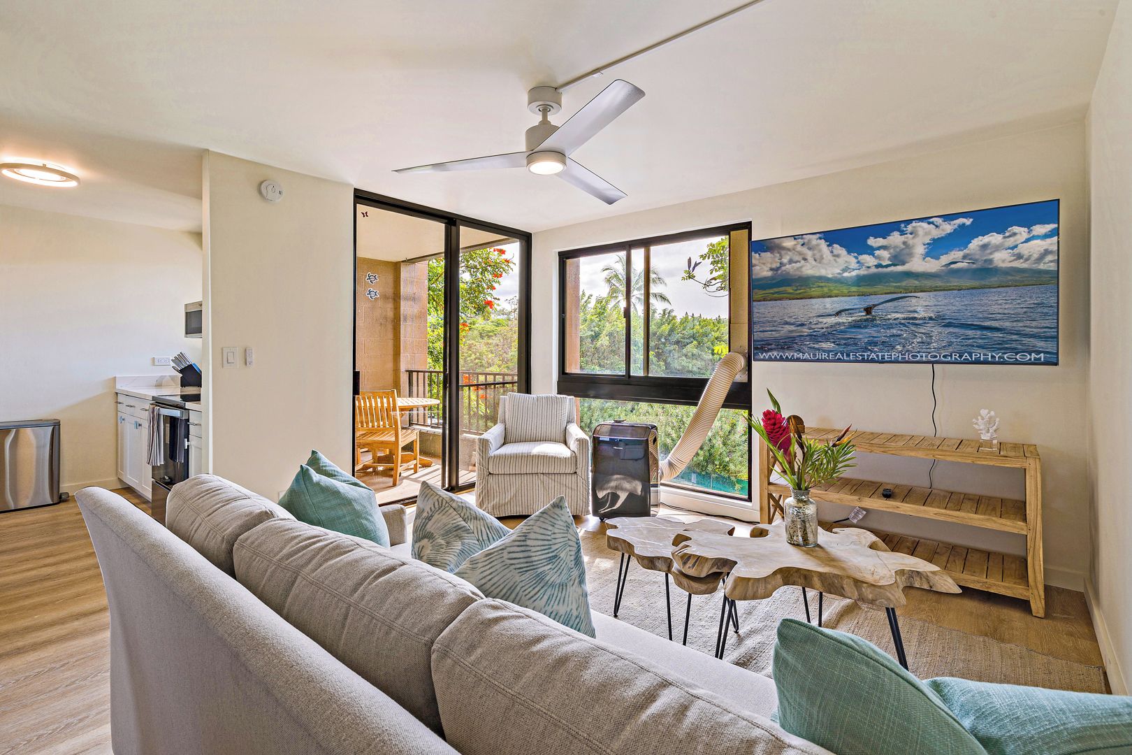 A modern living room with a sofa, a dining table, and a chair. There is a large window with a view of greenery and a painting on the wall.