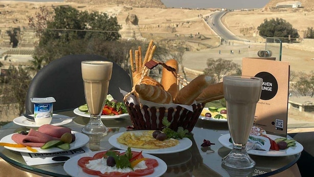 Un tavolo imbandito con cibo e bevande, affacciato su un paesaggio desertico con piramidi.