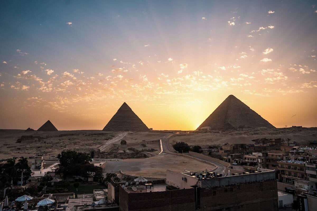 A view of the pyramids at sunset with a road leading to a settlement.