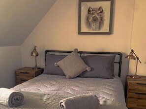 A bedroom with a bed, two nightstands, a framed picture on the wall, and a sloped ceiling. - Charming and Modern 3 bed Cottage in Wansford (Peterborough)