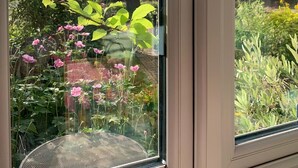 A window with a view of a garden, including pink flowers and green foliage. - Charming and Modern 3 bed Cottage in Wansford (Peterborough)