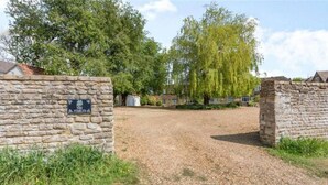 A gravel path leading to a stone wall with a sign reading "The Stables." - Charming and Modern 3 bed Cottage in Wansford (Peterborough)
