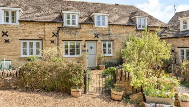 A stone house with multiple windows, a door, and a small garden with potted plants. - Charming and Modern 3 bed Cottage in Wansford (Peterborough)