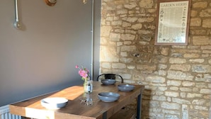 A rustic kitchen with a stone wall, a wooden table with bowls, and a vase with flowers. - Charming and Modern 3 bed Cottage in Wansford (Peterborough)