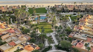 Un resort con varias edificaciones, una piscina central y vista al mar.