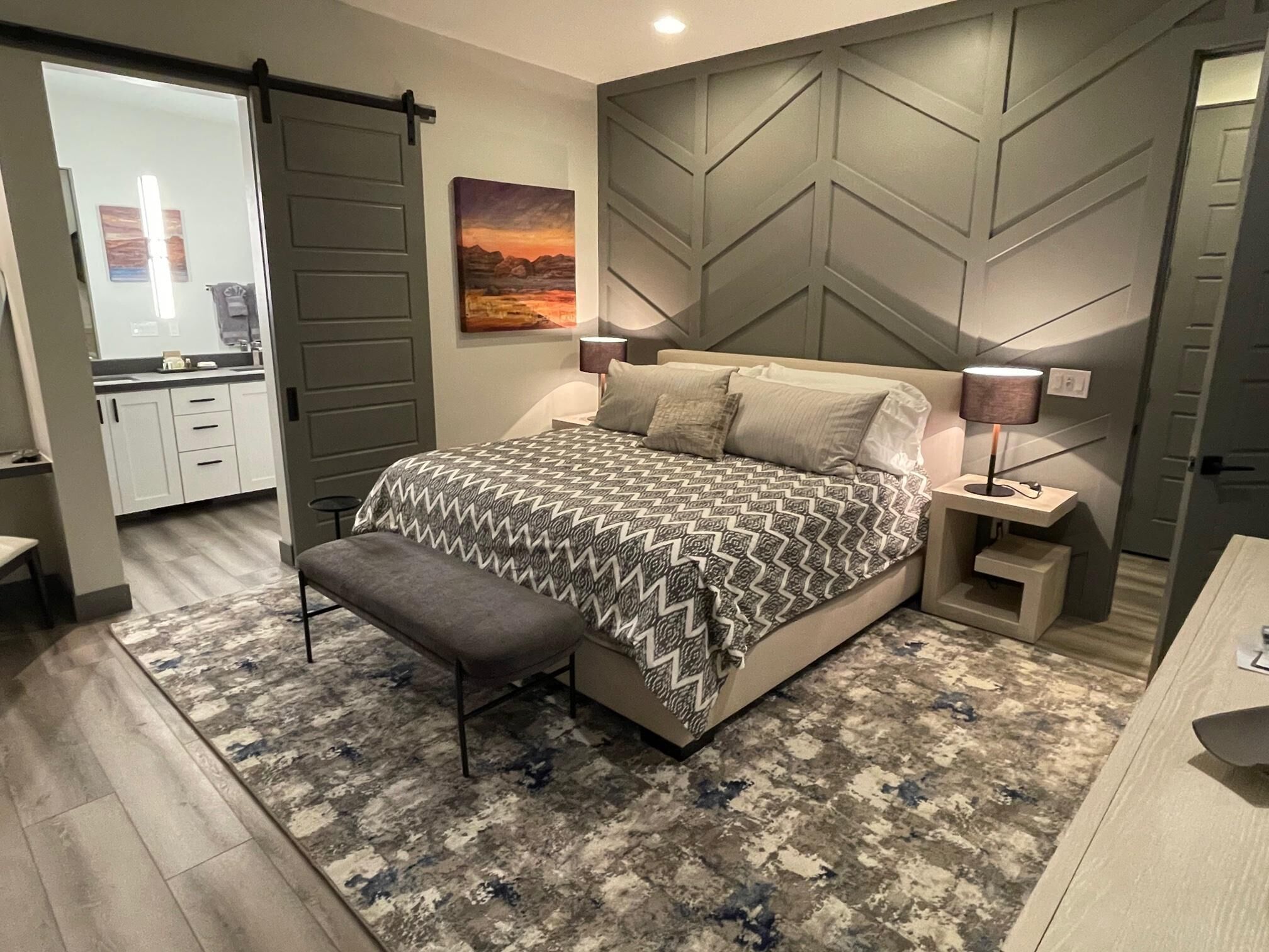 A modern bedroom with a large bed, a bench, a nightstand, and a wall-mounted lamp.