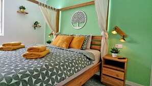 Ein ordentlich bezogenes Bett mit geometrischen Mustern und zwei Kissen, ein Nachttisch mit einer Pflanze und eine Wandleuchte.