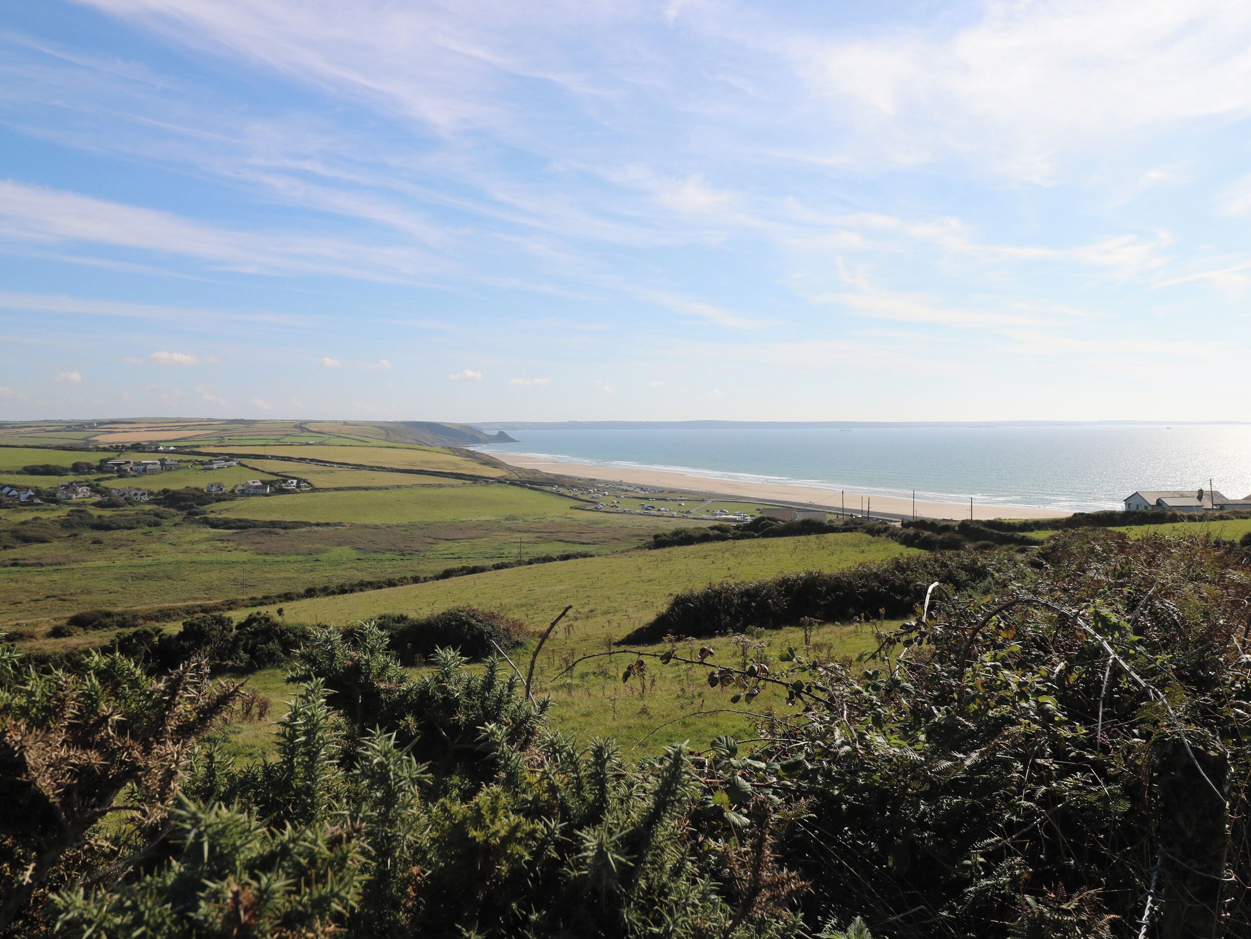 A coastal landscape with rolling green hills, a beach, and a clear sky.