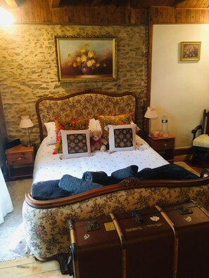 A bedroom with a floral-patterned bedspread, a wooden headboard, and a suitcase on the floor.